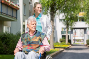 Woman assisting a senior man in a wheelchair outside of a multi-family home.