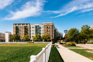 Multi-family housing architecture featuring a grassy landscape with benches and a walking path.