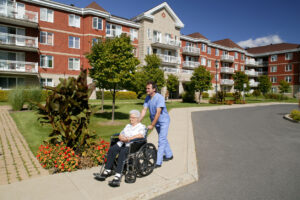 Male caregiver assisting a senior woman in a wheelchair outside of a multi-family home.