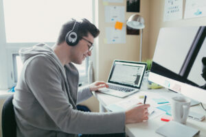 Male college student studying in his room using a computer and a laptop - student housing architecture concept.